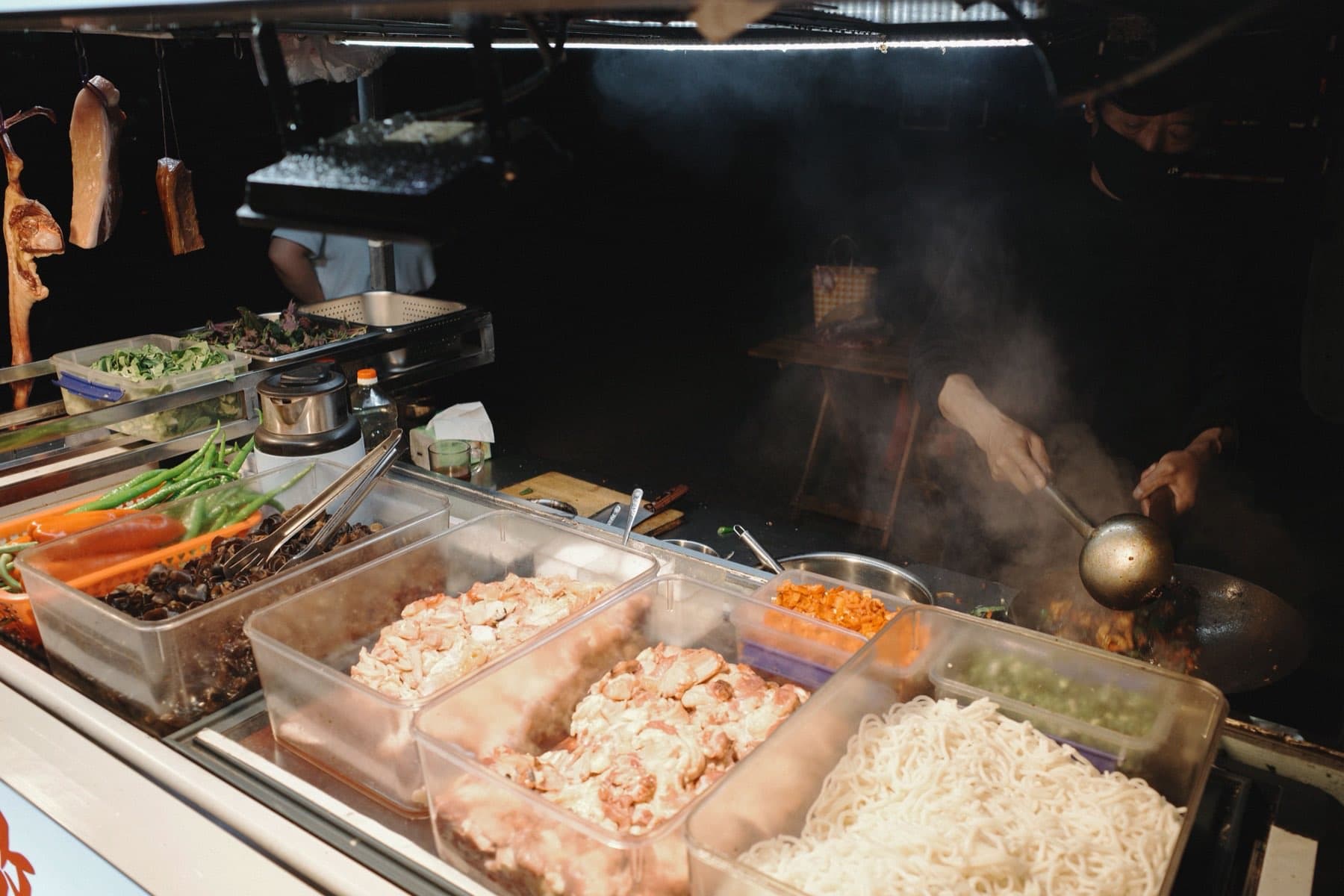 Hanging meats and steam rising from a wok at a street food stall